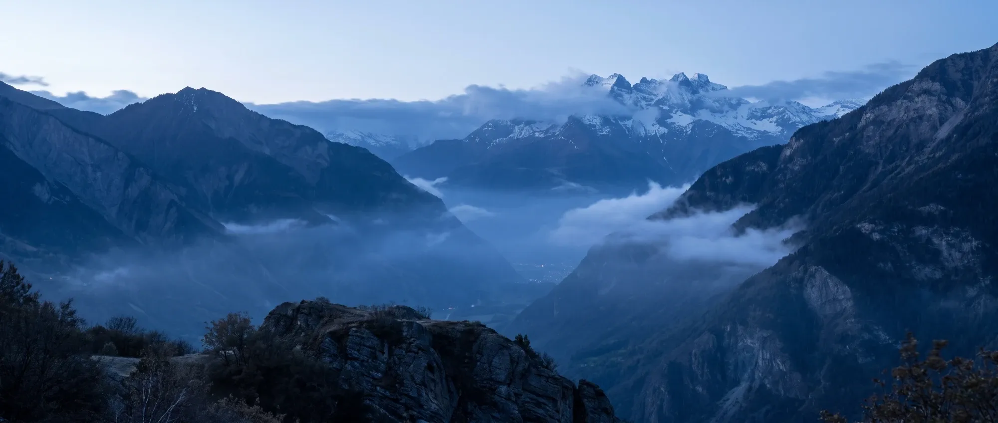 Vallée alpine au crépuscule, brume et sommets enneigés